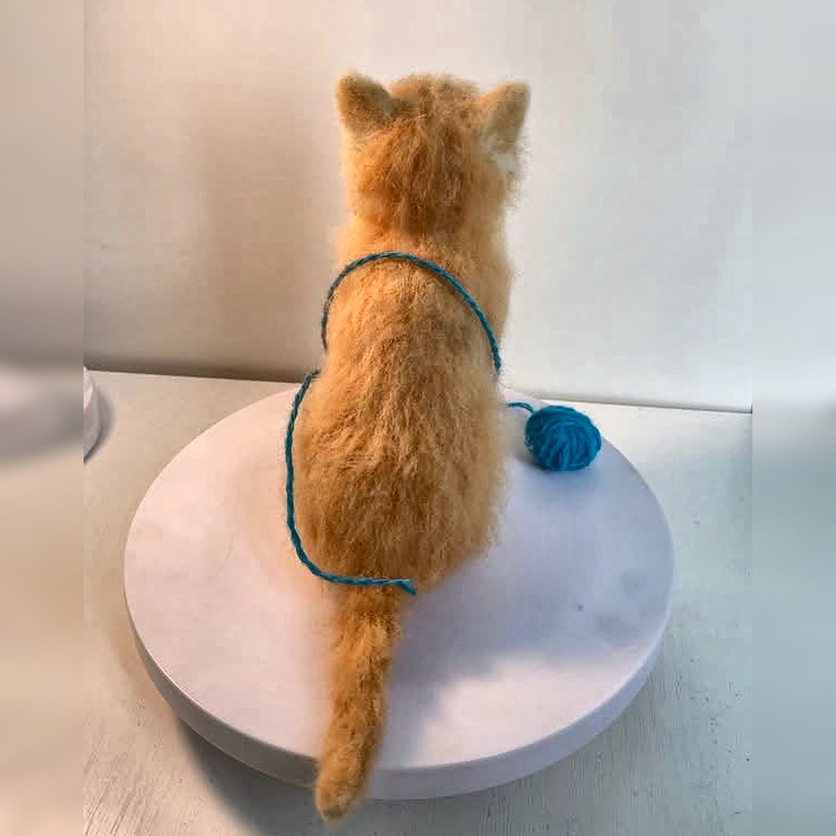 Back view of the ginger kitten felt sculpture, showing its ears and tail; square image