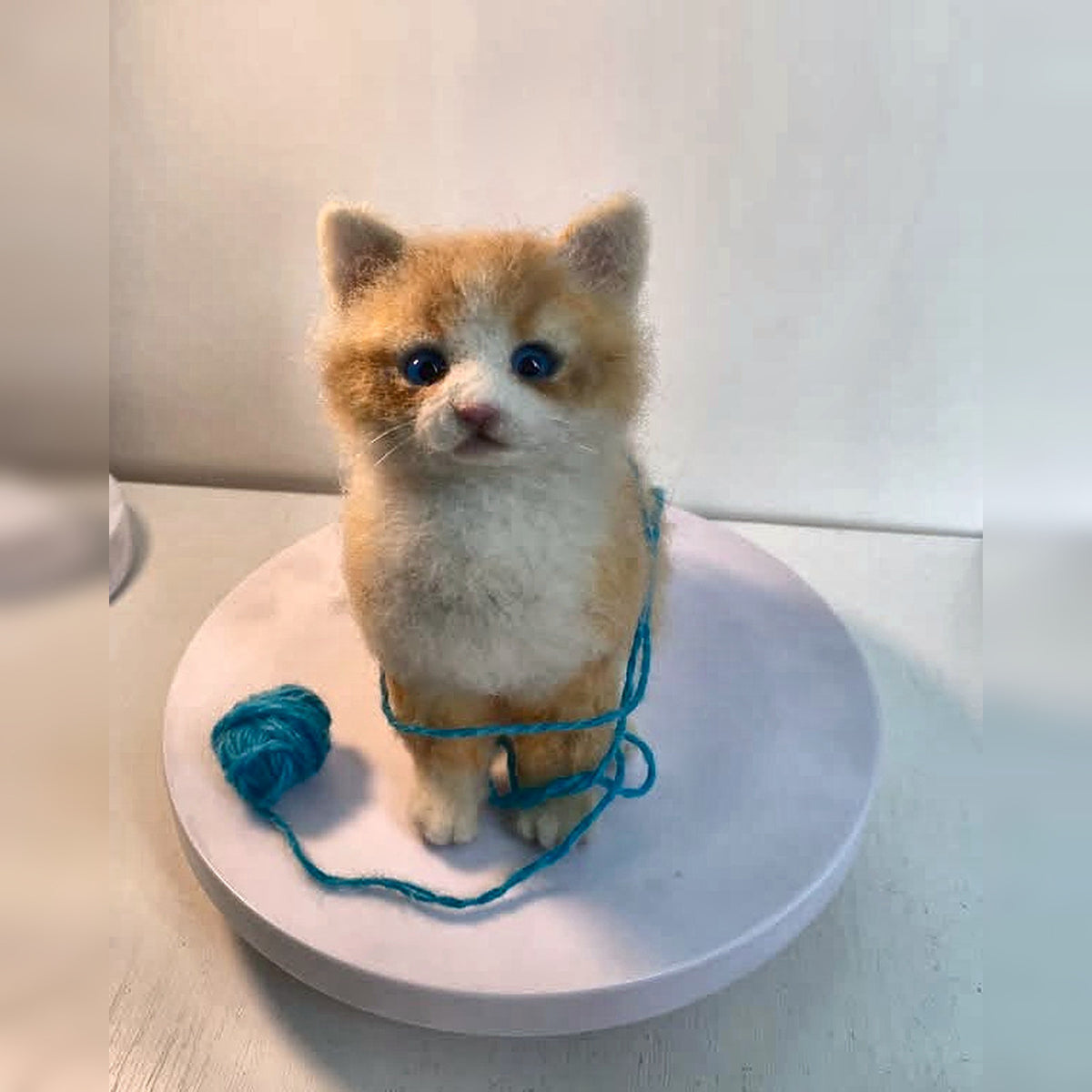 Finished ginger-and-cream felt kitten sculpture photographed from the front beside blue yarn; square image