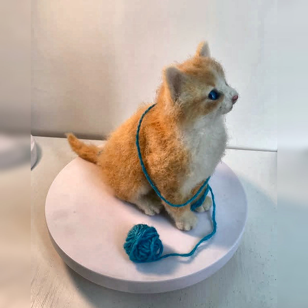 Left-side view of the ginger-and-cream felt kitten with a blue yarn ball; square image