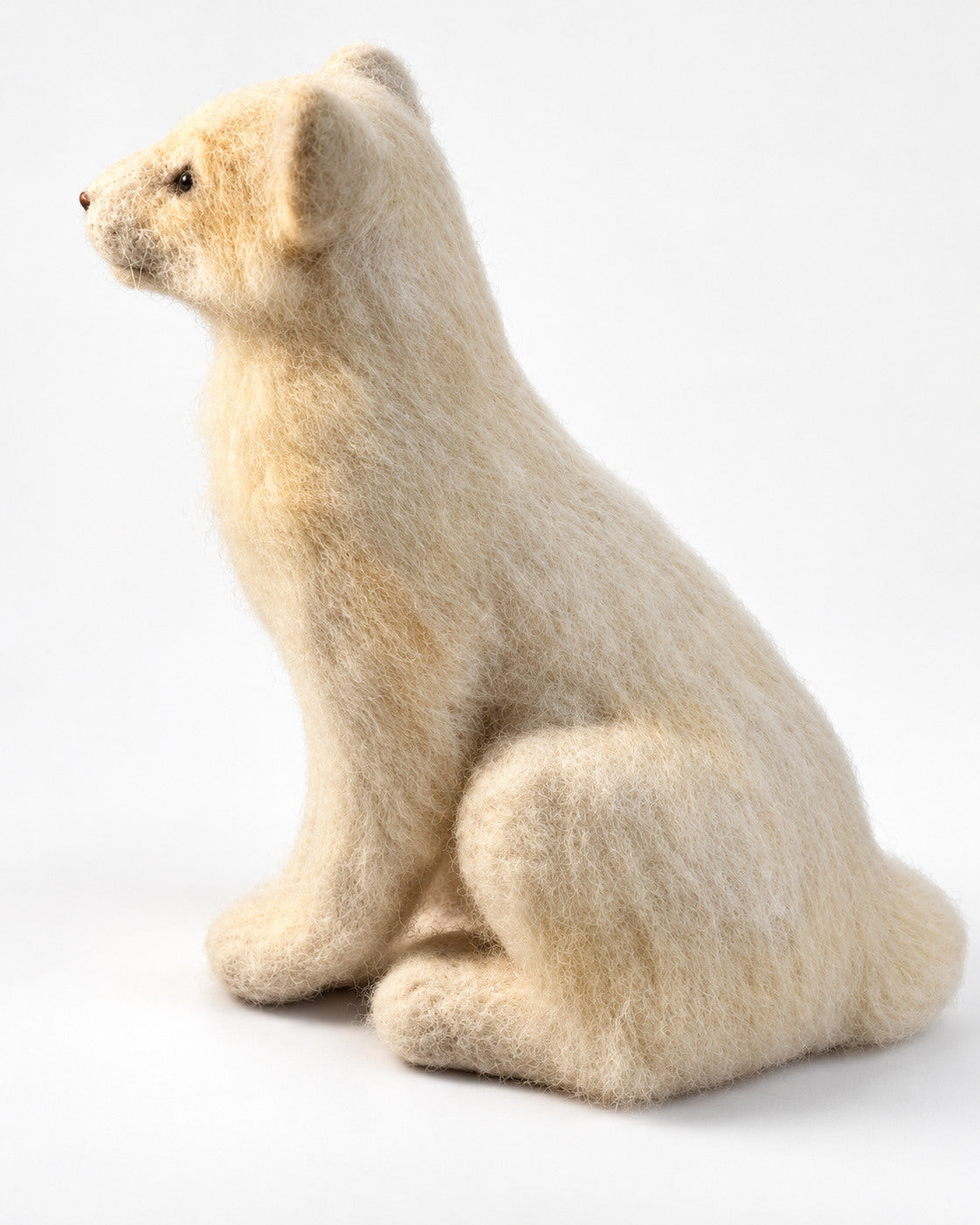 Profile of the white felt lion cub sculpture showing its nose, small paws and long curled tail